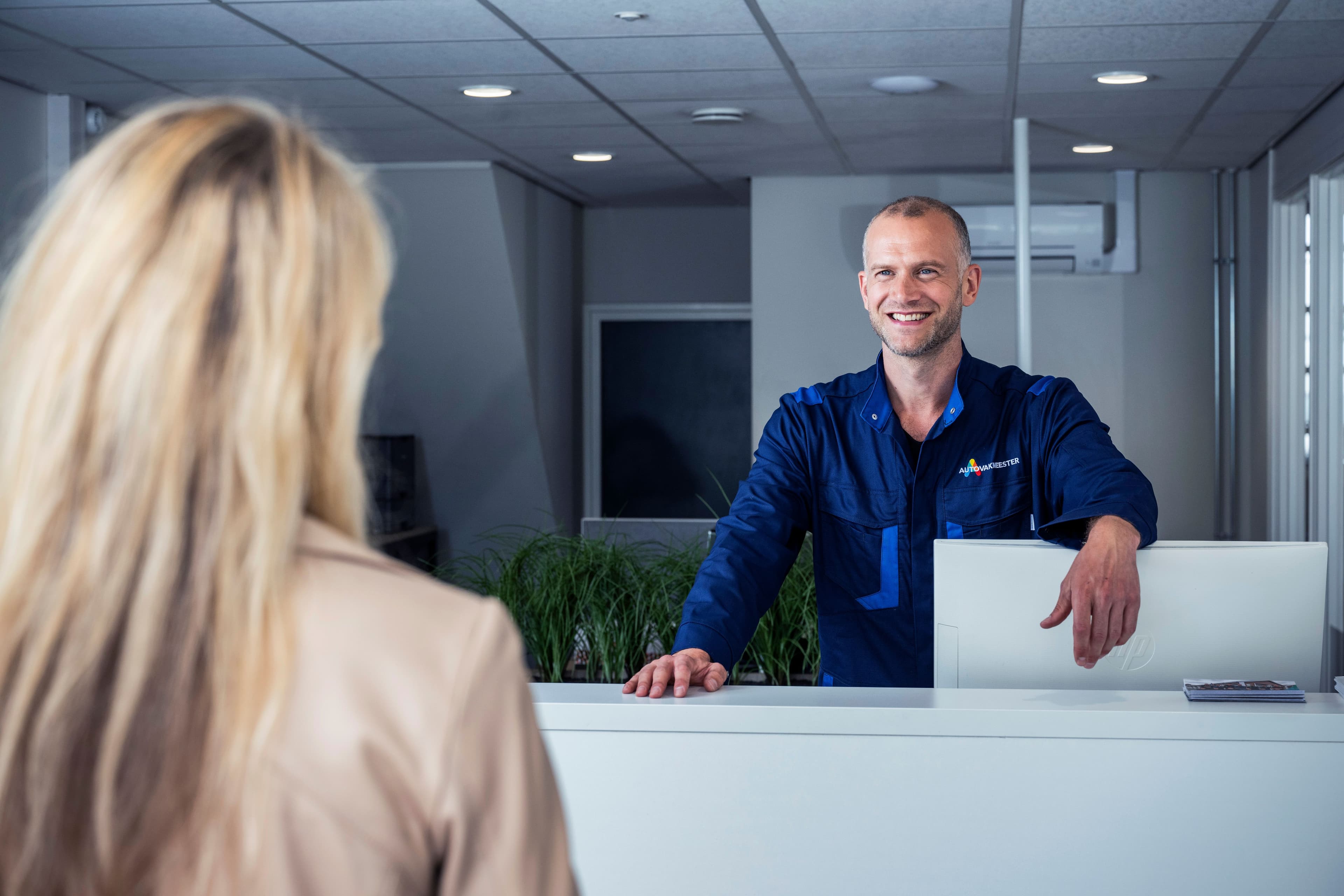 Autorepairmaster ontvangt klant aan de balie.
